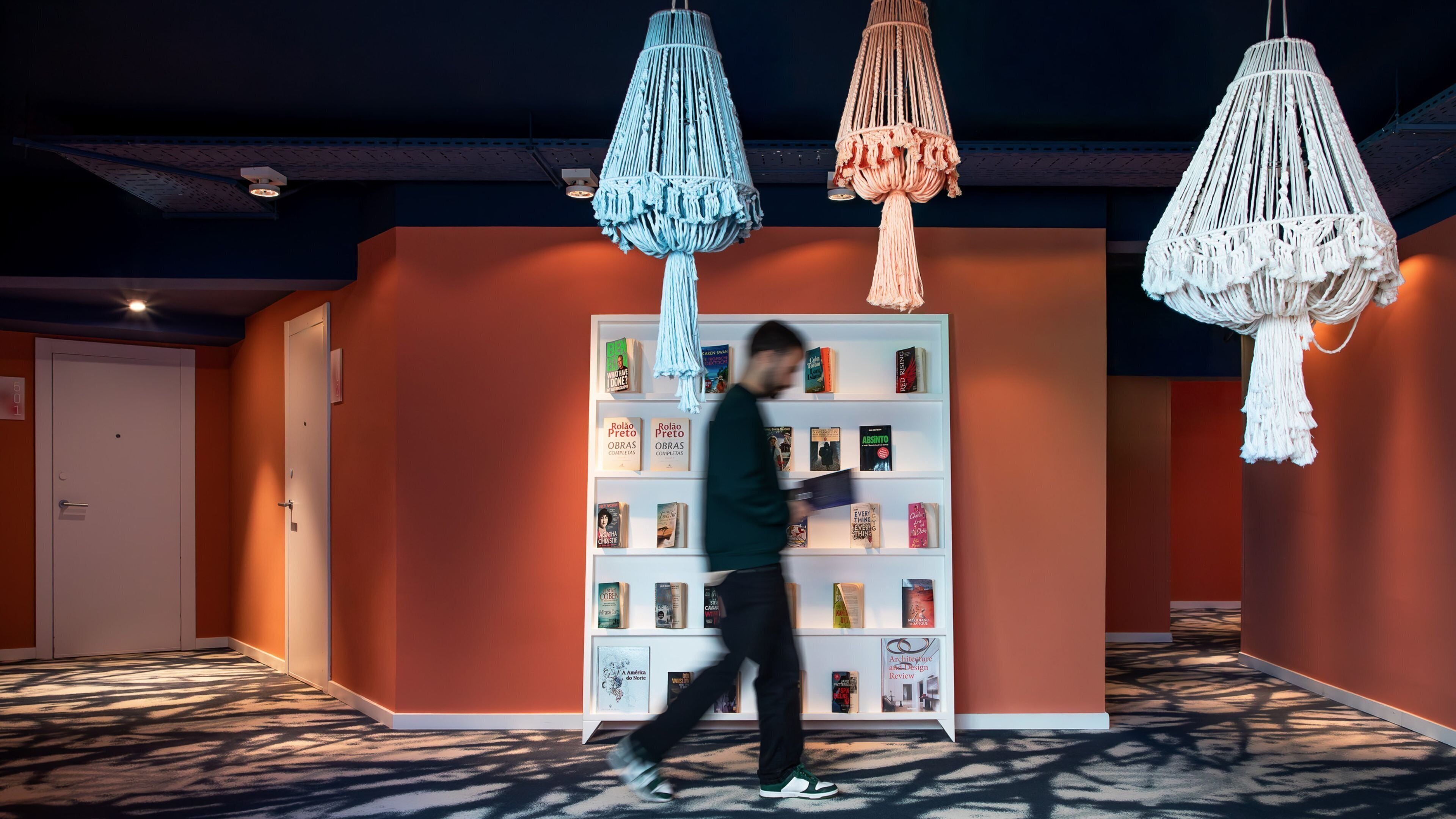 A modern interior with a white bookshelf filled with books, a patterned carpet, and macramé wall hangings.