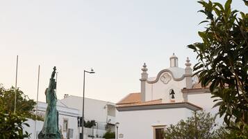 A white building with a bell tower and a statue in front.