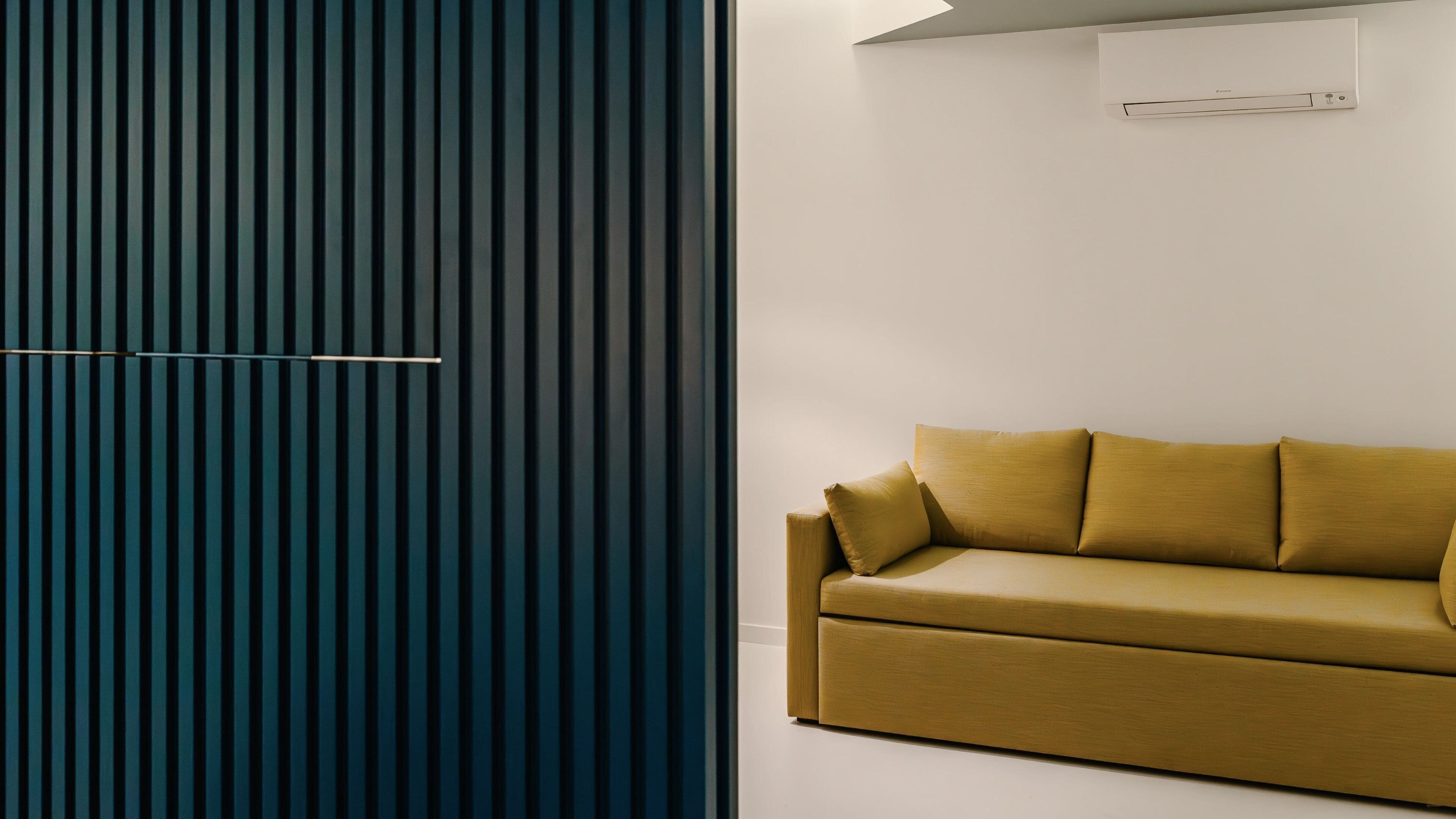 A modern room with a dark blue vertical panel wall, a beige sofa with cushions, and a white ceiling with an air conditioning unit.