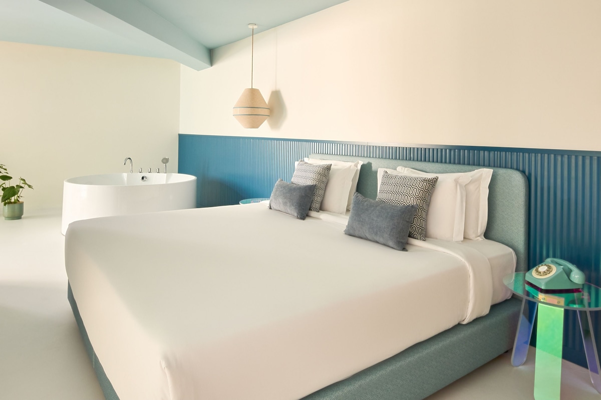 Un dormitorio moderno con una cama grande, una bañera y una mesita con un teléfono.