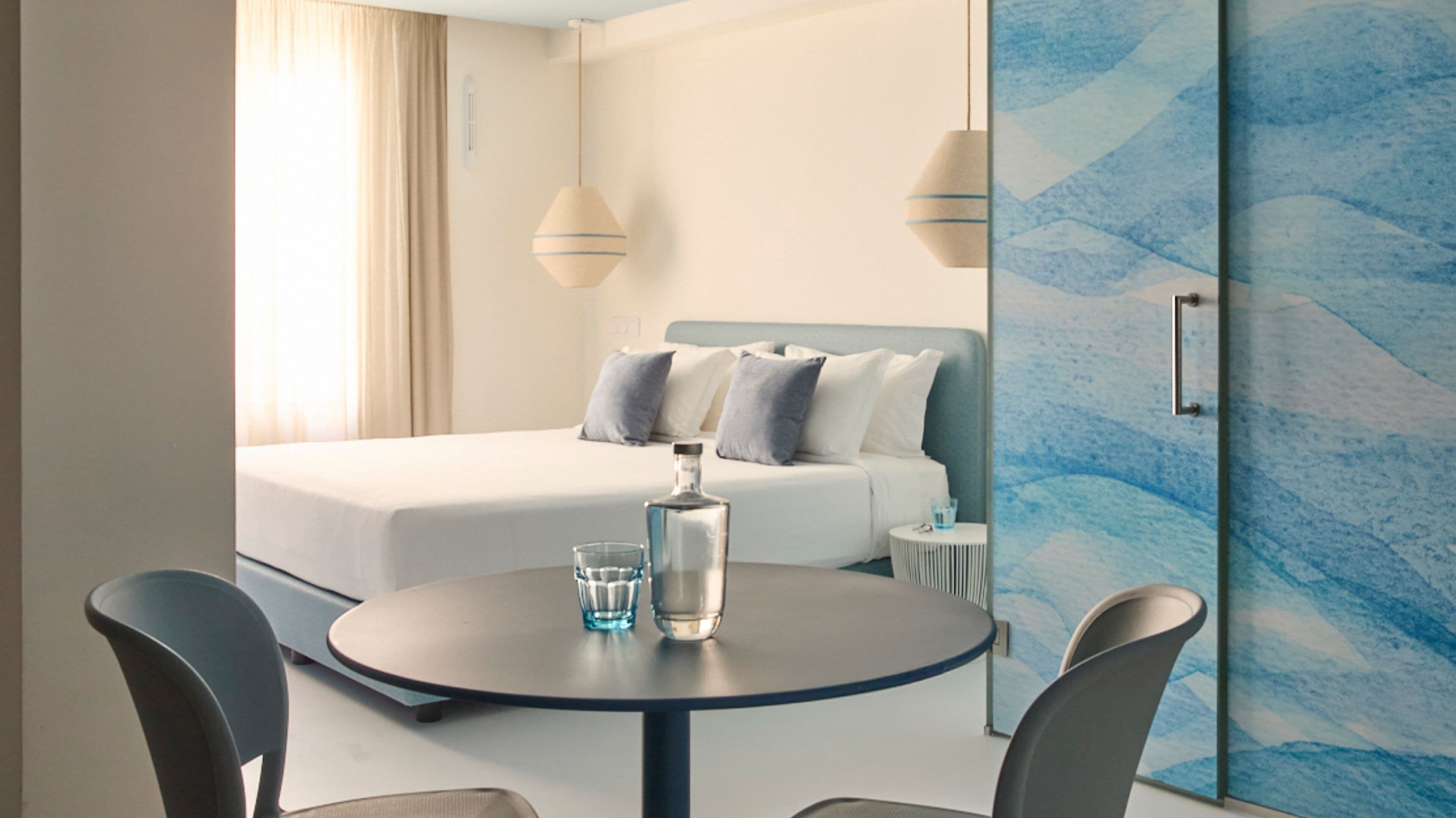 Habitación de hotel con cama, mesita de noche y una mesa redonda con sillas.