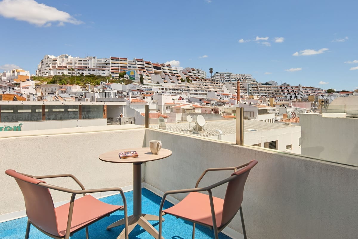 A rooftop terrace with a pool, two chairs, and a table.