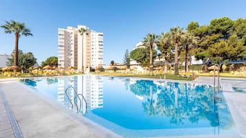 Una piscina al aire libre, sombrillas, sillones reclinables de piscina