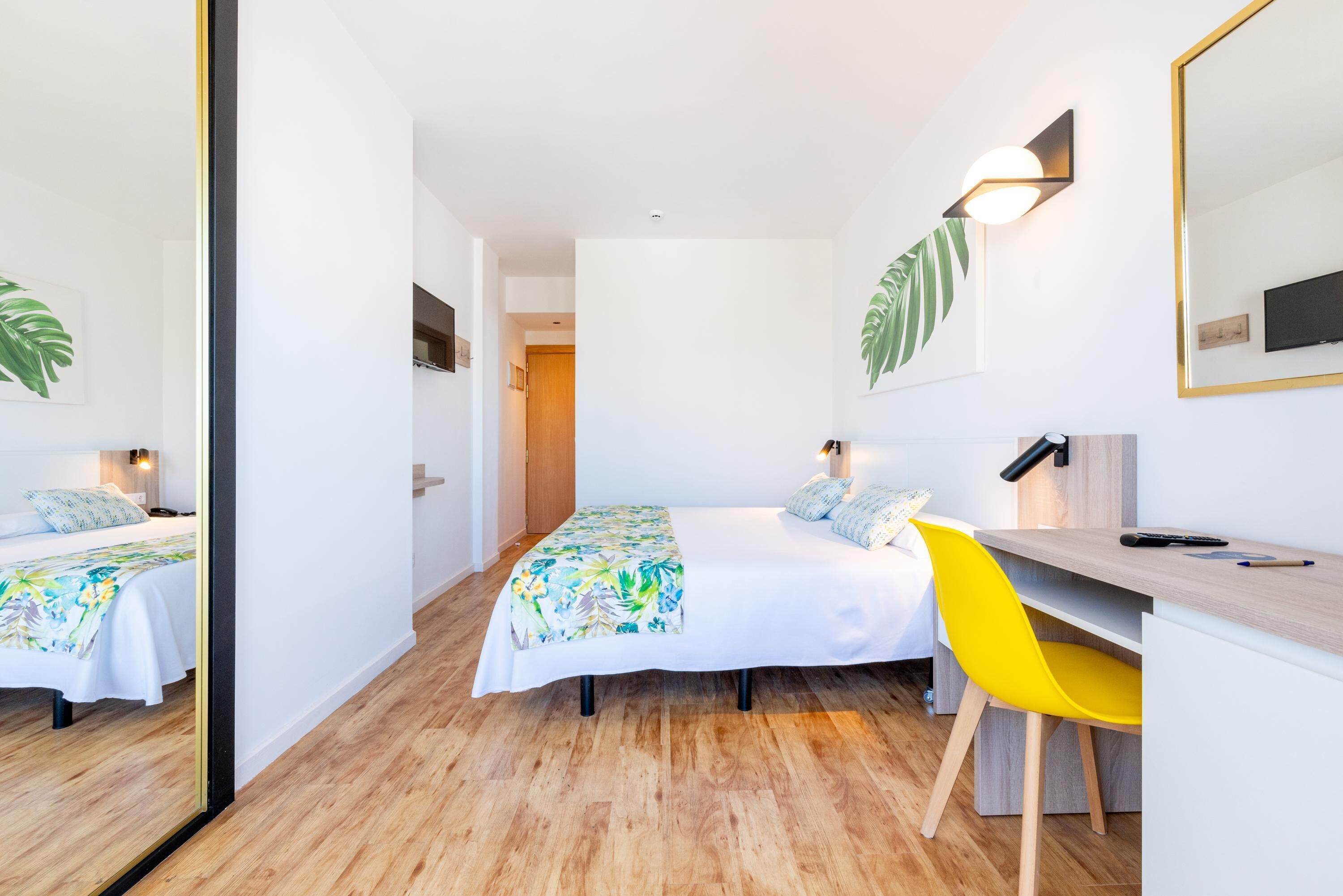 Una habitación de hotel moderna con cama, escritorio, silla y espejo.