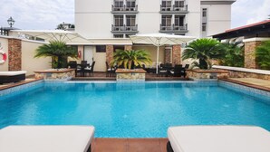 A swimming pool with lounge chairs and umbrellas, surrounded by stone walls and potted plants. - BON Hotel Abuja (Abuja)