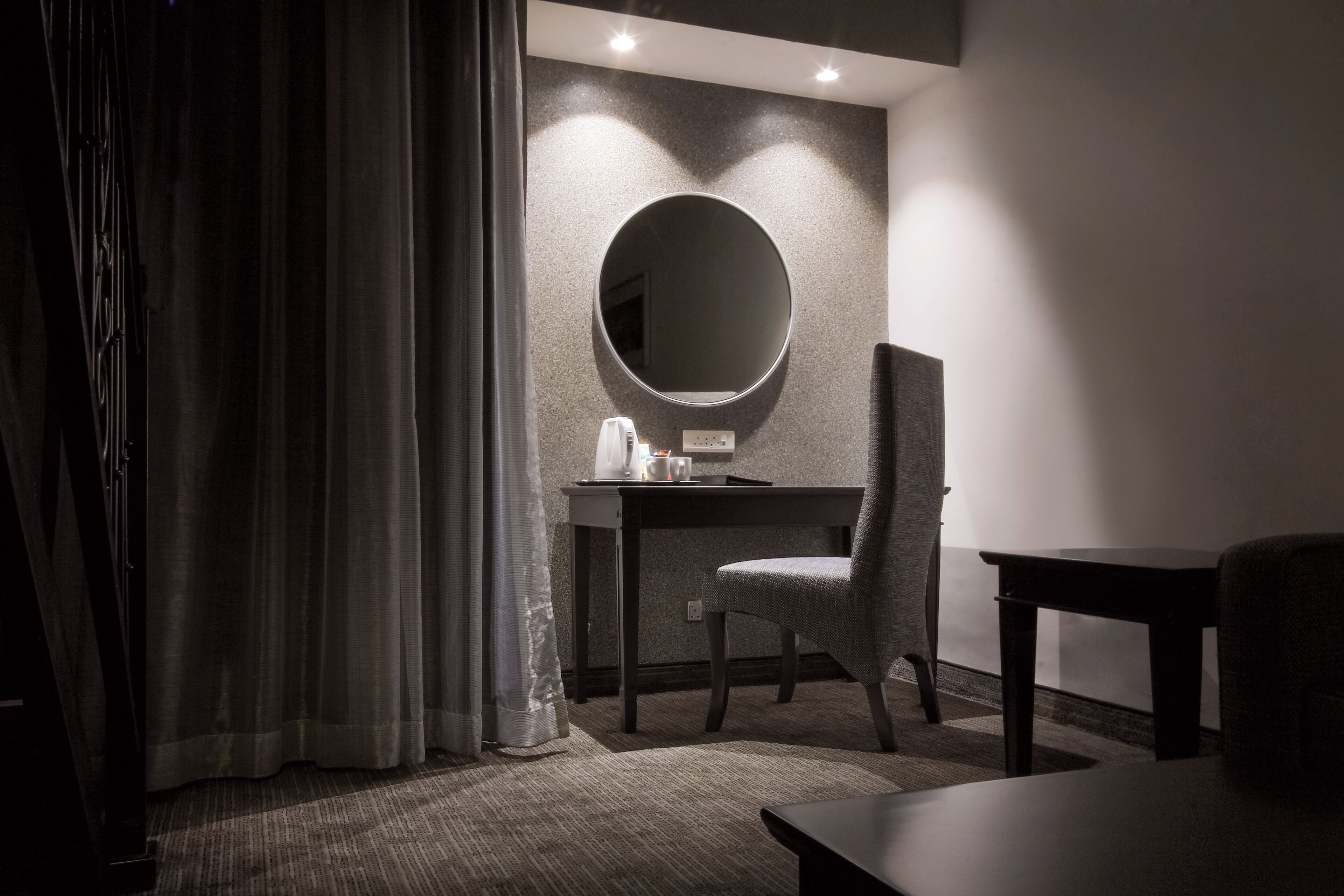 A hotel room with a desk, chair, and a round mirror on the wall.