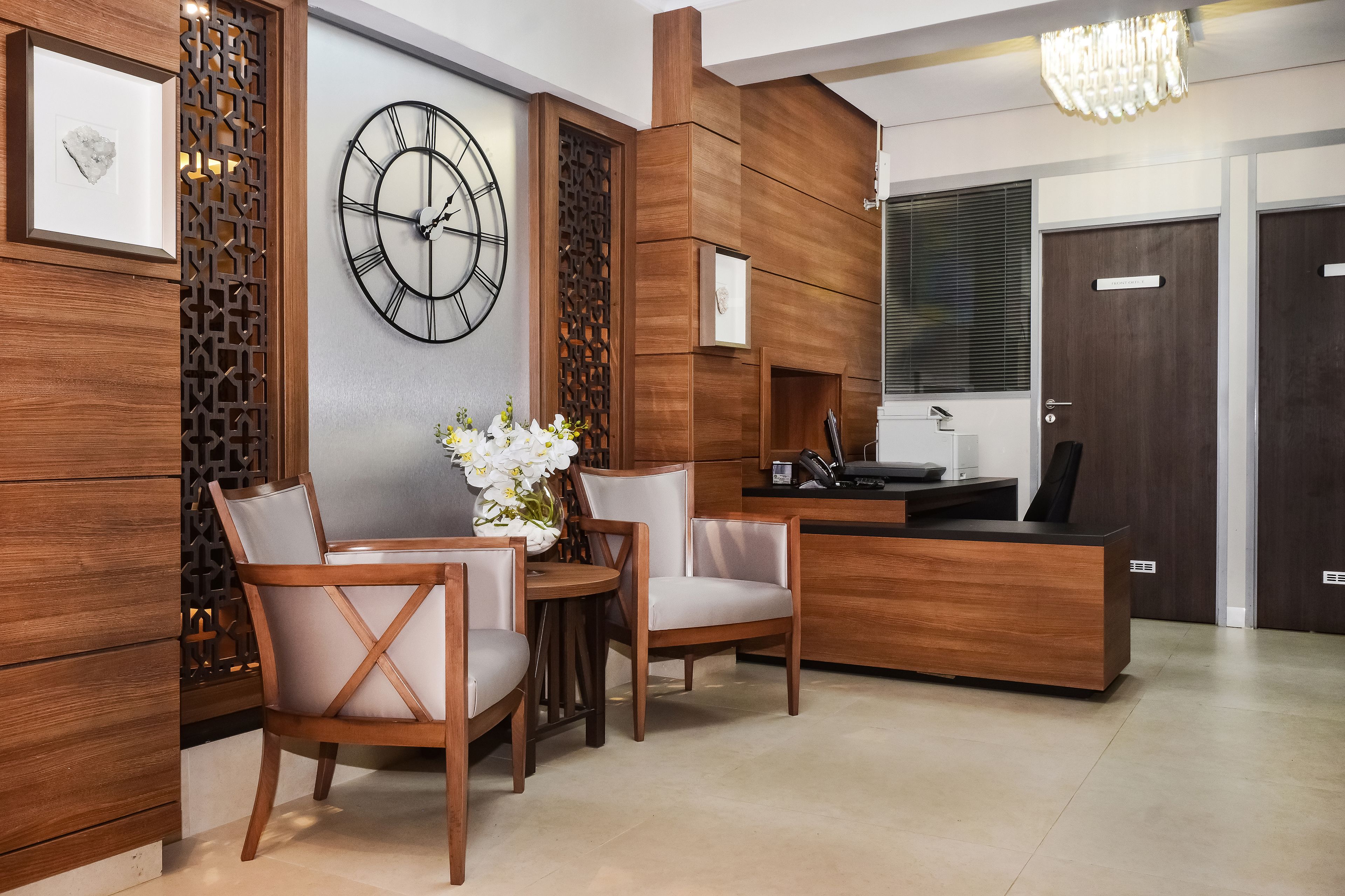 Una zona de recepción moderna con un mostrador de madera, dos sillas, un reloj y un panel decorativo.