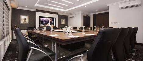 A conference room with a long table, black chairs, and a television screen.