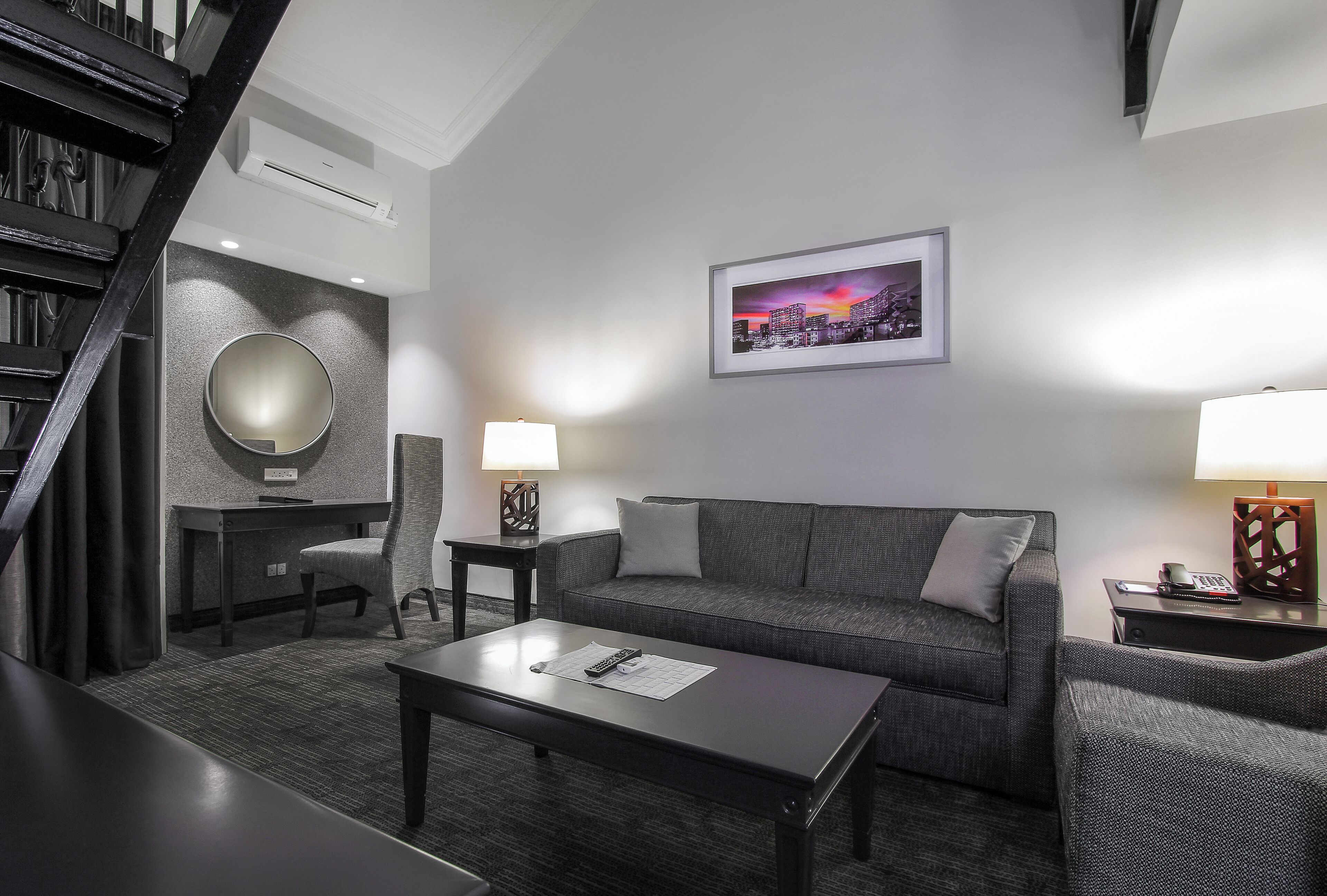 Een moderne hotelkamer met een grijze bank, een ronde spiegel, een eettafel en een stadsbeeld aan de muur.