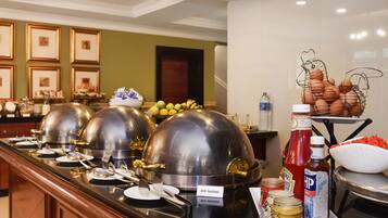 A buffet setup with multiple food stations, including a beef sausage station, condiments, and a fruit bowl.