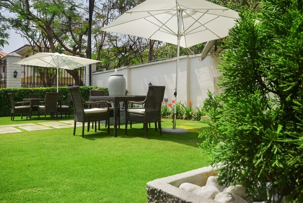 A patio with a dining table and chairs, surrounded by a well-maintained lawn and a white wall.