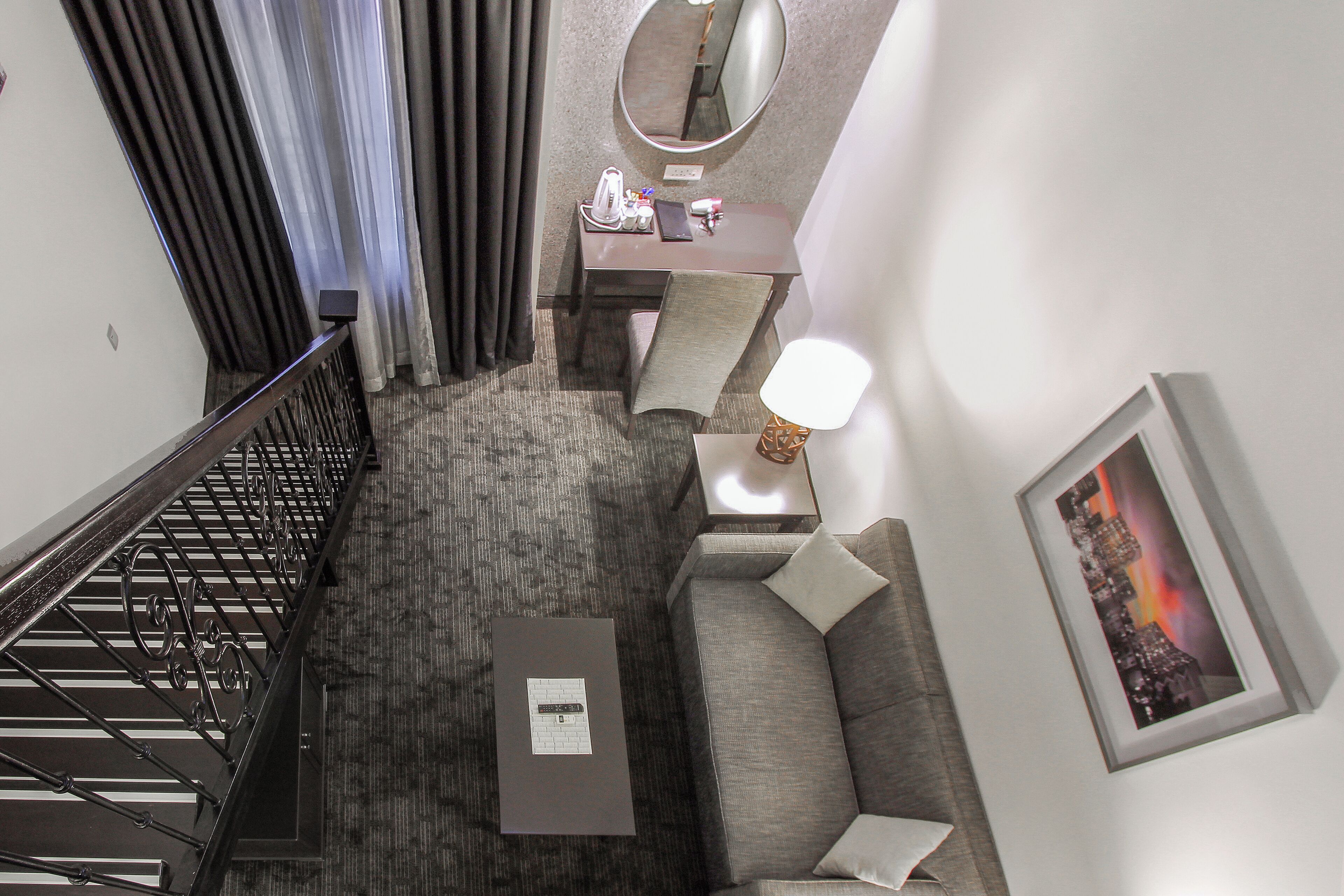 A hotel room with a staircase, a desk with a mirror, a sofa, a small table, and a framed picture on the wall.