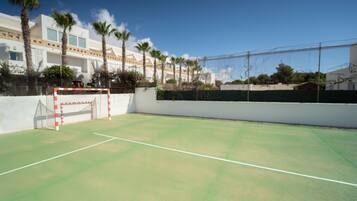A tennis court with a goal post, palm trees, and a building in the background.