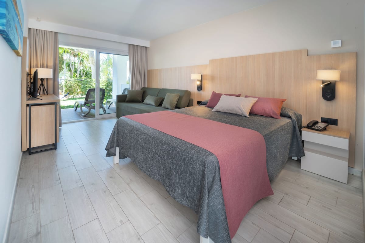 Habitación de hotel moderna con una cama grande, un sofá, un escritorio con lámpara y vistas al exterior.