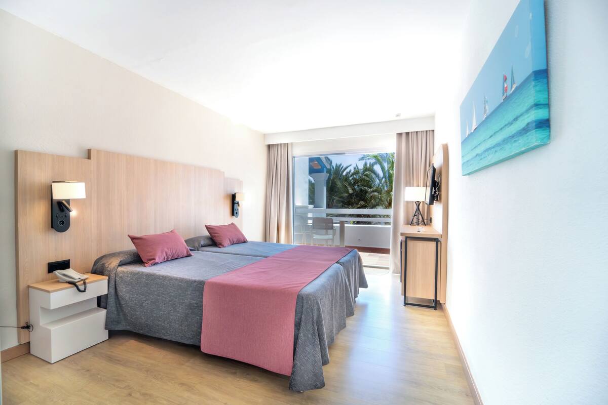 Habitación de hotel con una cama grande, un escritorio, una silla y un balcón con vistas al mar.