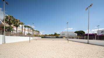 Una cancha de voleibol de playa con arena, paredes blancas y palmeras.