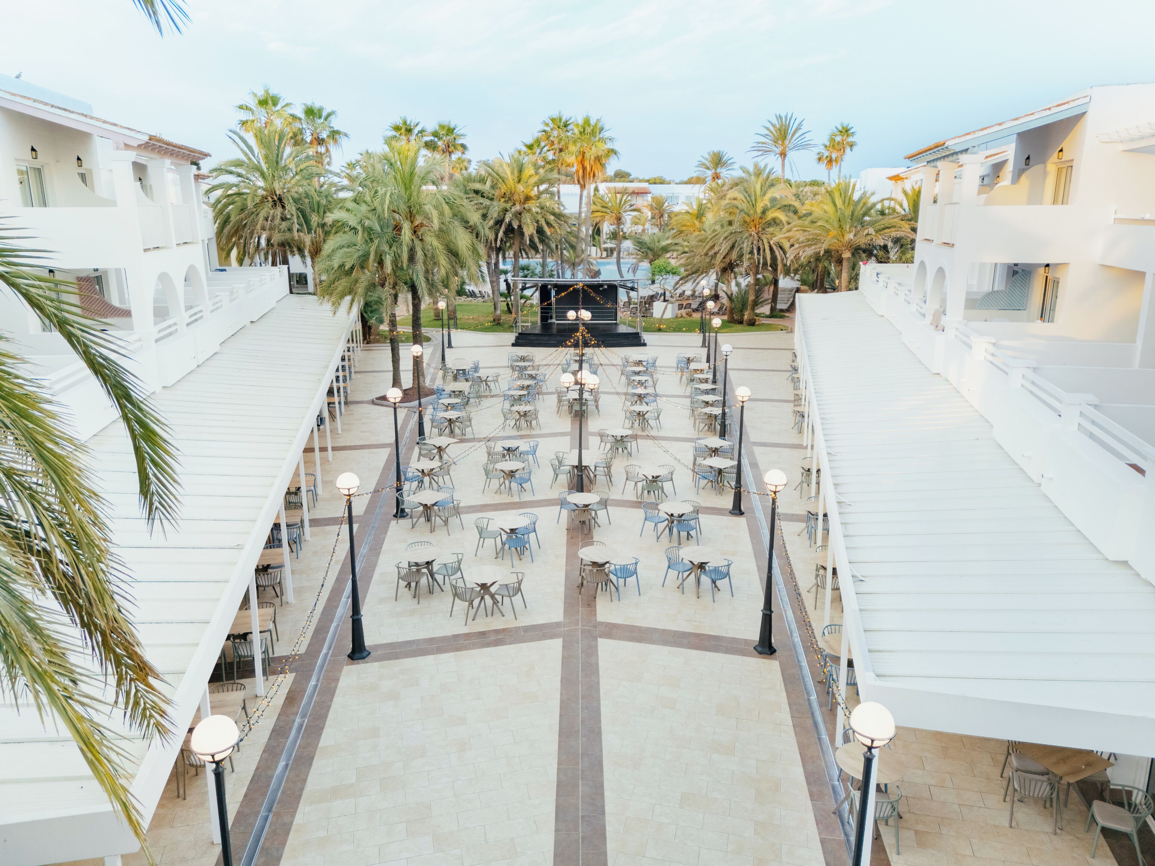 Terraza en la azotea con mobiliario exterior, palmeras y un escenario para eventos.