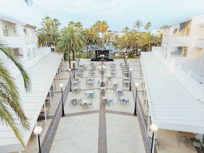 A rooftop terrace with outdoor seating, palm trees, and a stage for events.