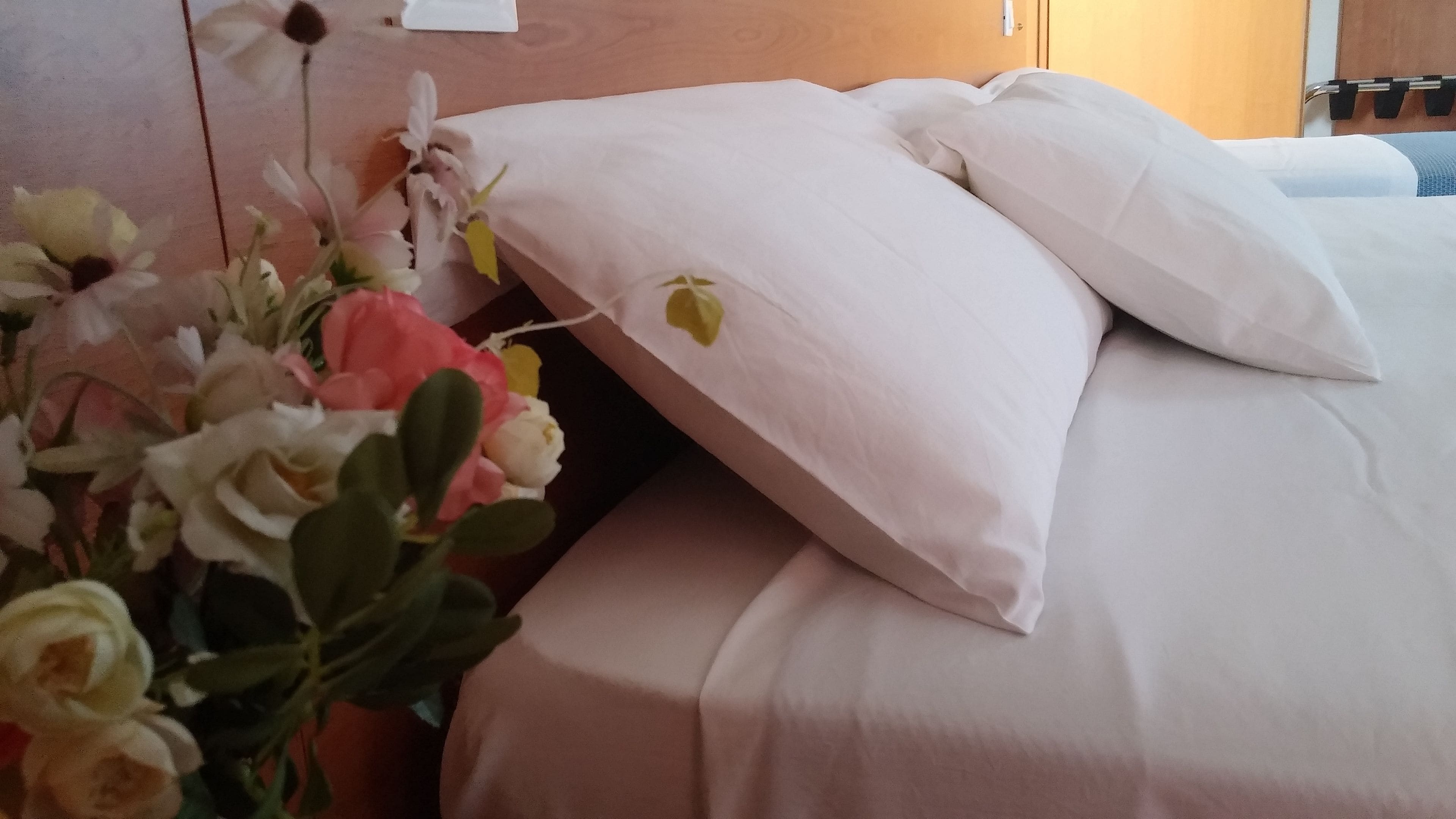 A neatly made bed with white linens and a single yellow flower on the pillow.