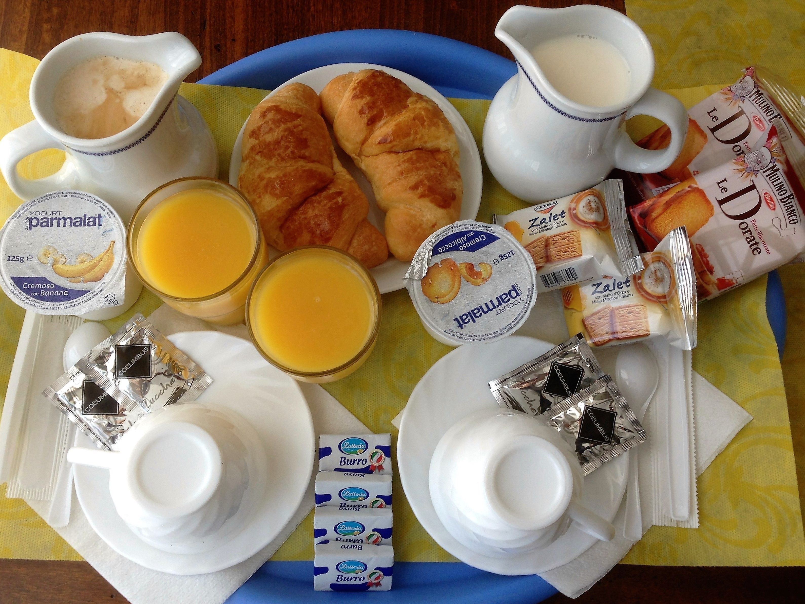 A breakfast tray with croissants, yogurt, juice, and coffee.