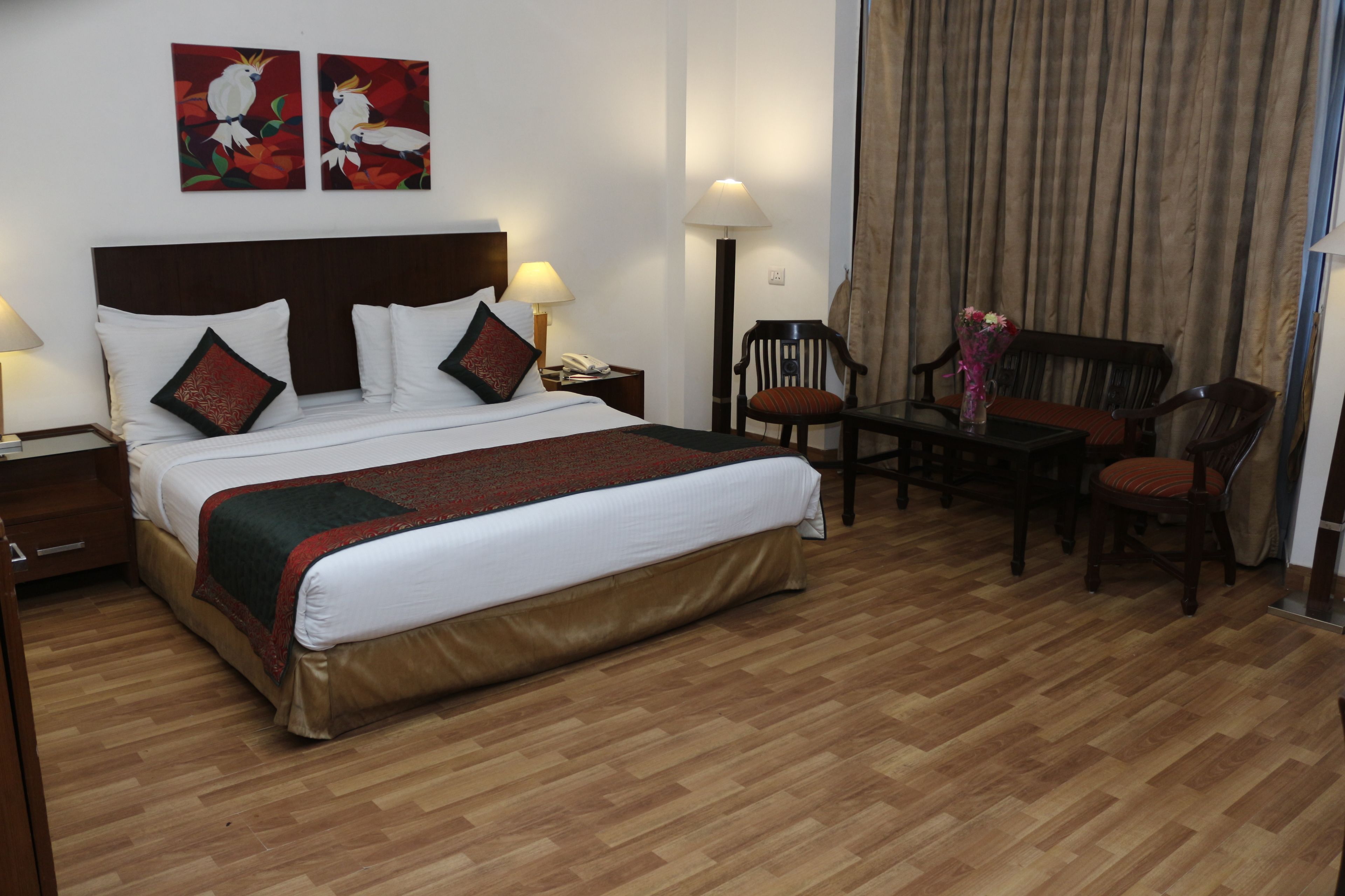 A hotel room with a large bed, two bedside tables with lamps, a desk with a chair, and a window with curtains.