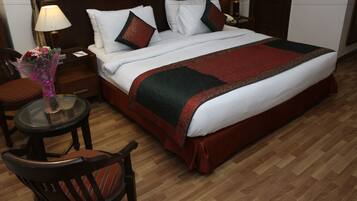Una habitación de hotel con una cama grande, dos lámparas de noche, una mesita redonda con un florero y una silla.