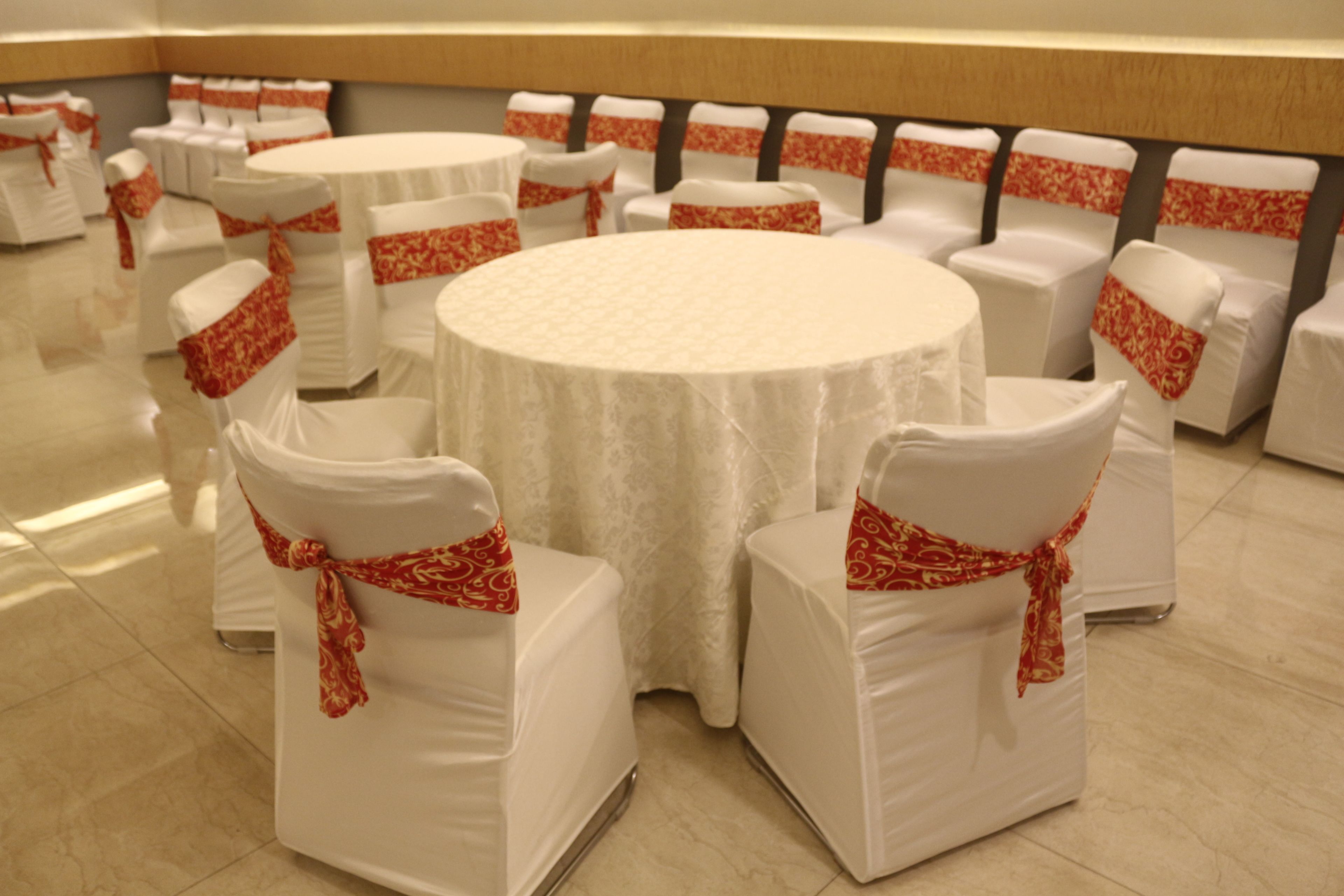 Une salle de conférence avec des tables rondes et des chaises blanches ornées de rubans rouges.