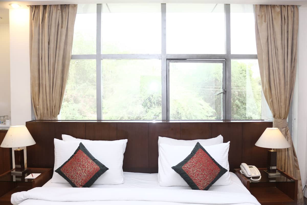 A hotel room with a large window, two bedside tables with lamps, a bed with white bedding and decorative pillows, and a telephone on the right table.