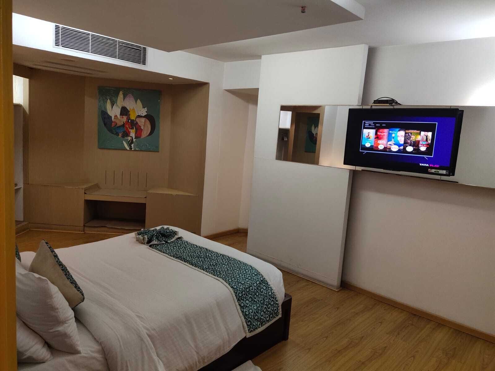 Une chambre d’hôtel avec un lit, un téléviseur fixé au mur, un tableau au mur et un petit coin salon.
