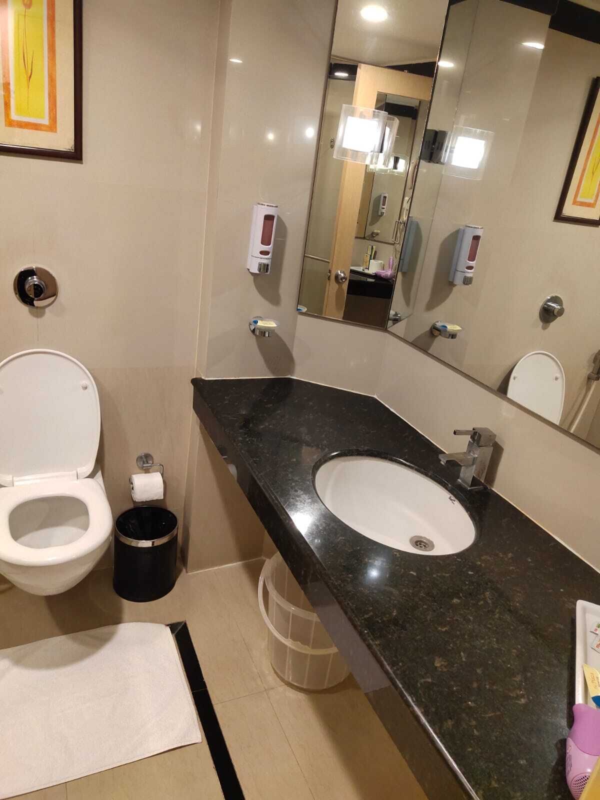 A modern bathroom with a white toilet, a black sink, and a large mirror.