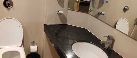 A modern bathroom with a white toilet, a black sink, and a large mirror.