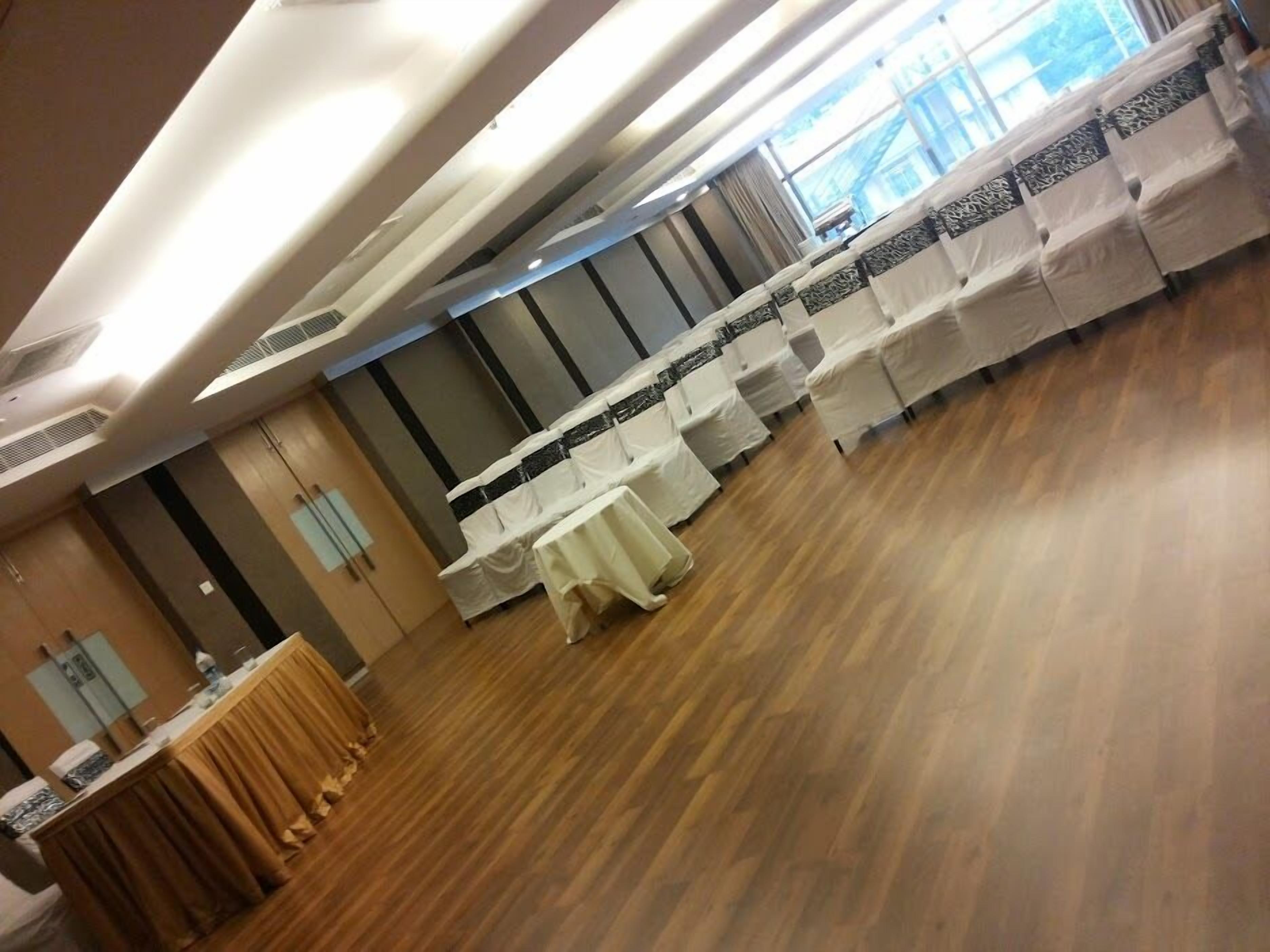 Een vergaderruimte met tafels bedekt met witte tafelkleden, een houten vloer en een groot raam met uitzicht op gebouwen.