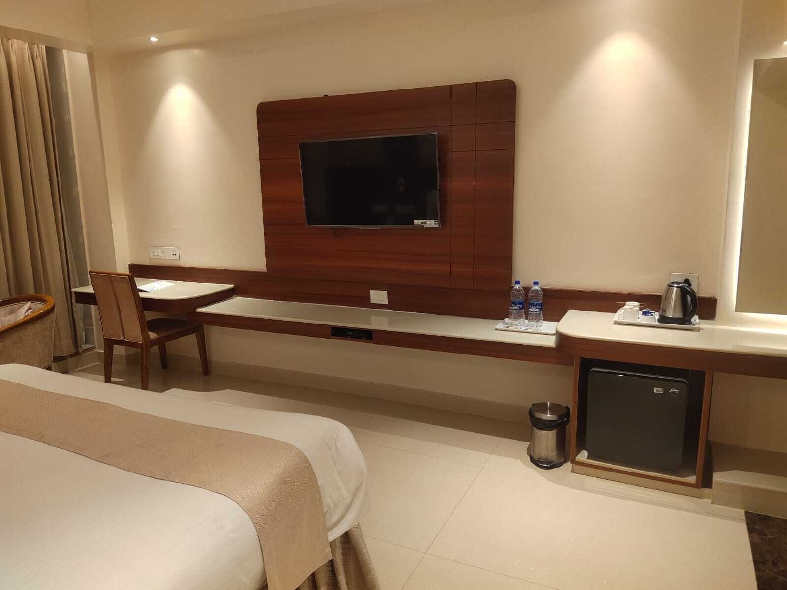 A hotel room with a bed, a desk, a chair, a television mounted on the wall, a coffee maker, and a mini-fridge.