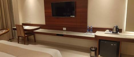 A hotel room with a bed, a desk, a chair, a television mounted on the wall, a coffee maker, and a mini-fridge.