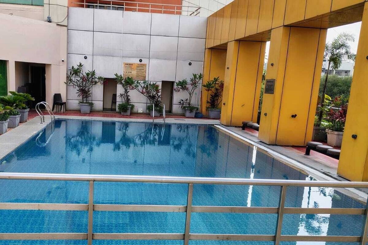 A swimming pool with a tiled deck, surrounded by potted plants and a yellow structure.