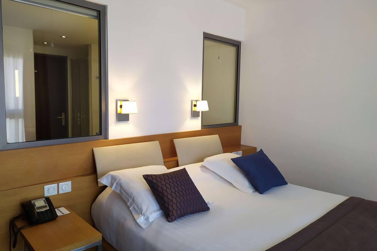 A hotel room with a bed, bedside tables, a phone, and wall-mounted lamps.