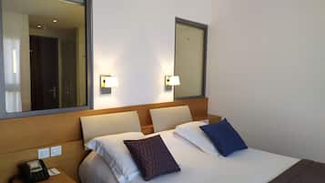 Una habitación de hotel con cama, mesitas de noche, teléfono y lámparas de pared.