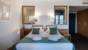 Un cuarto de hotel con una cama grande, dos mesitas de noche, dos lámparas, un espejo y vistas a la ciudad desde la ventana.