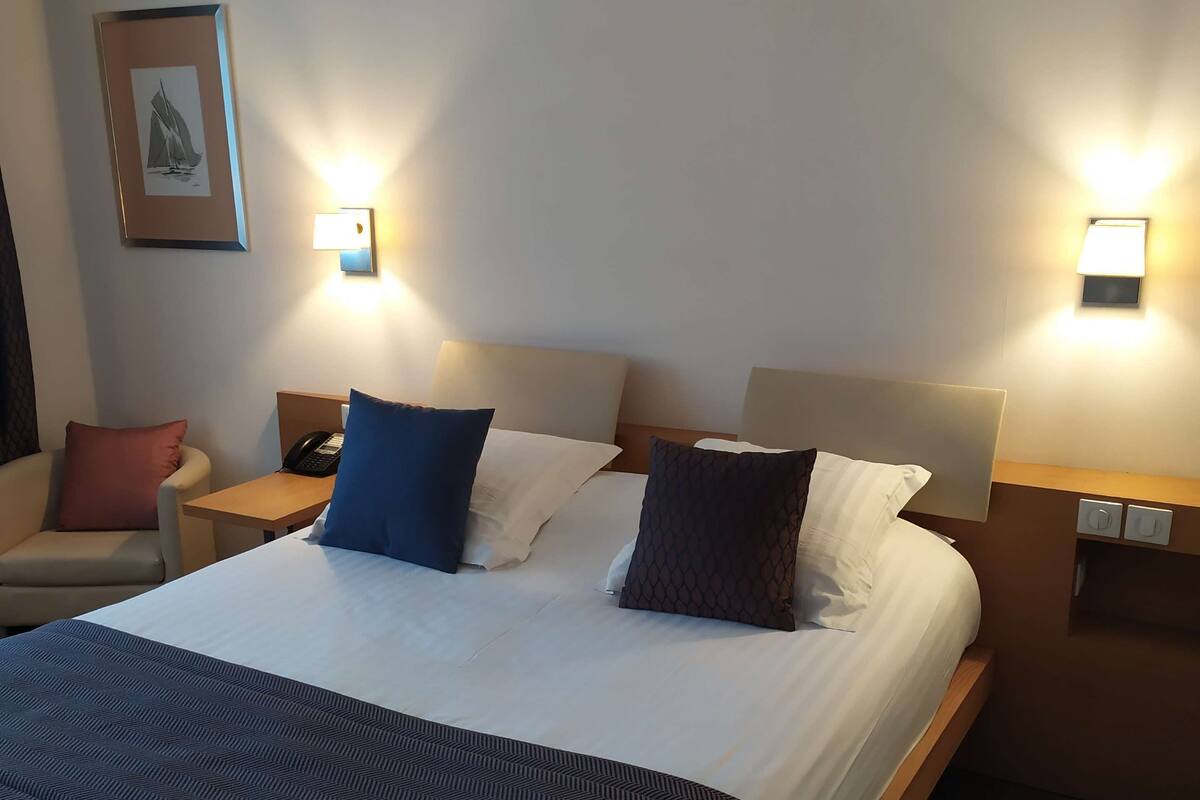 A hotel room with a large bed, two bedside tables, a chair, and a wall-mounted lamp.