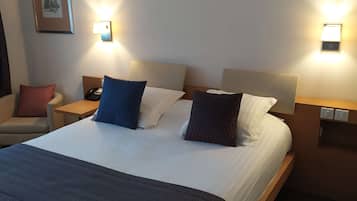 Une chambre d’hôtel avec un grand lit, deux tables de chevet, une chaise et une lampe fixée au mur.