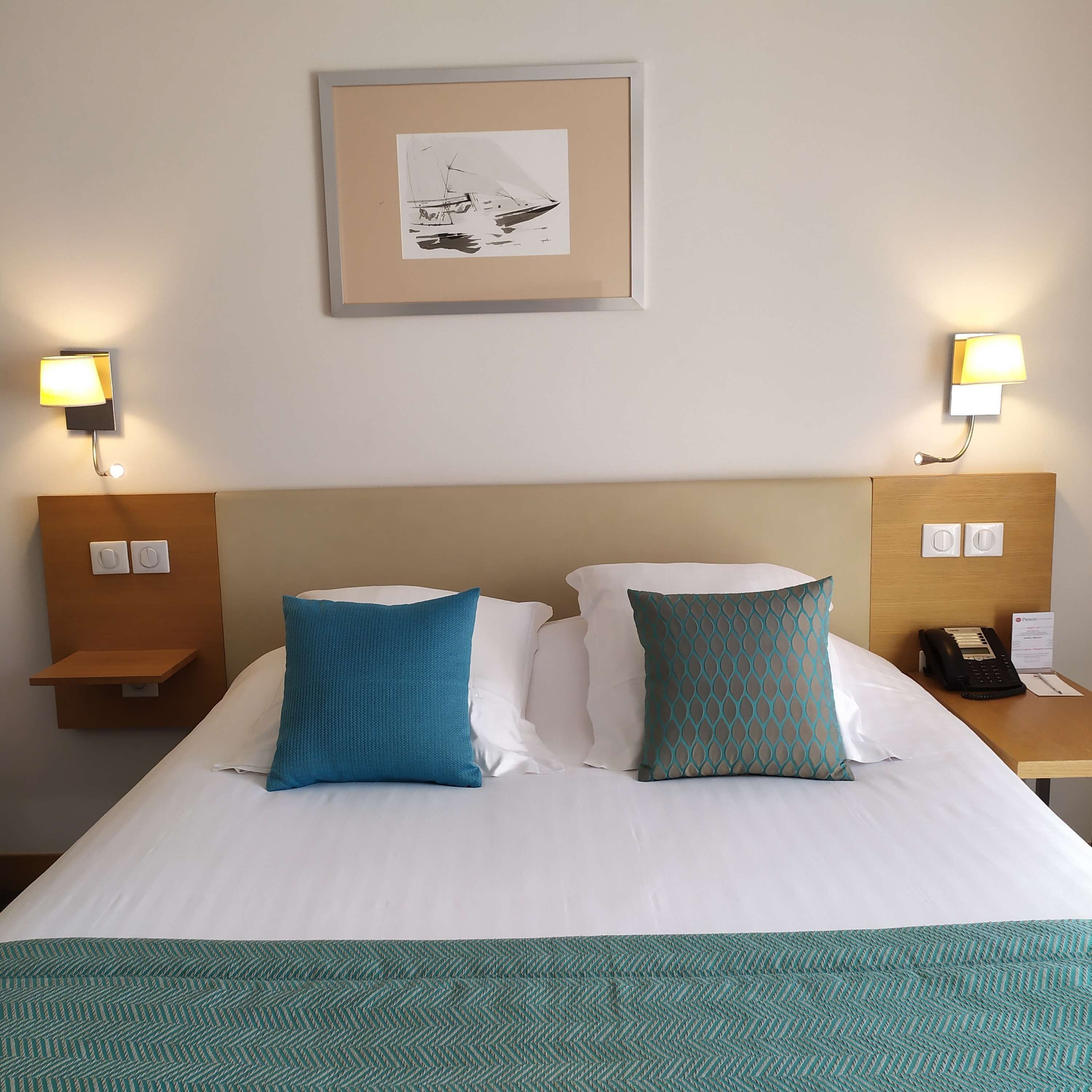 A hotel room with a large bed, two pillows, a framed picture on the wall, and bedside lamps.