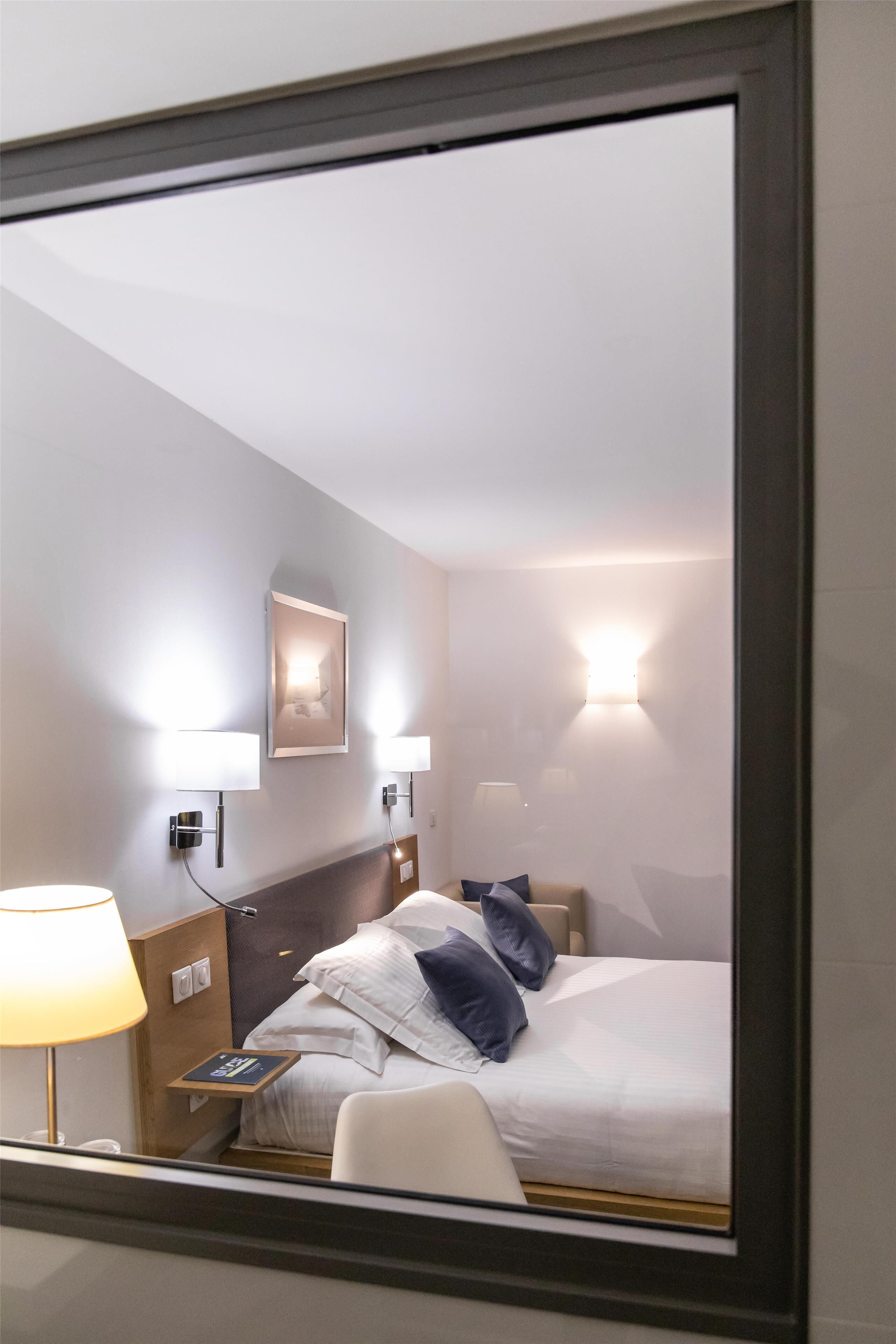 A hotel room with a bed, bedside lamp, and a wall-mounted light fixture.