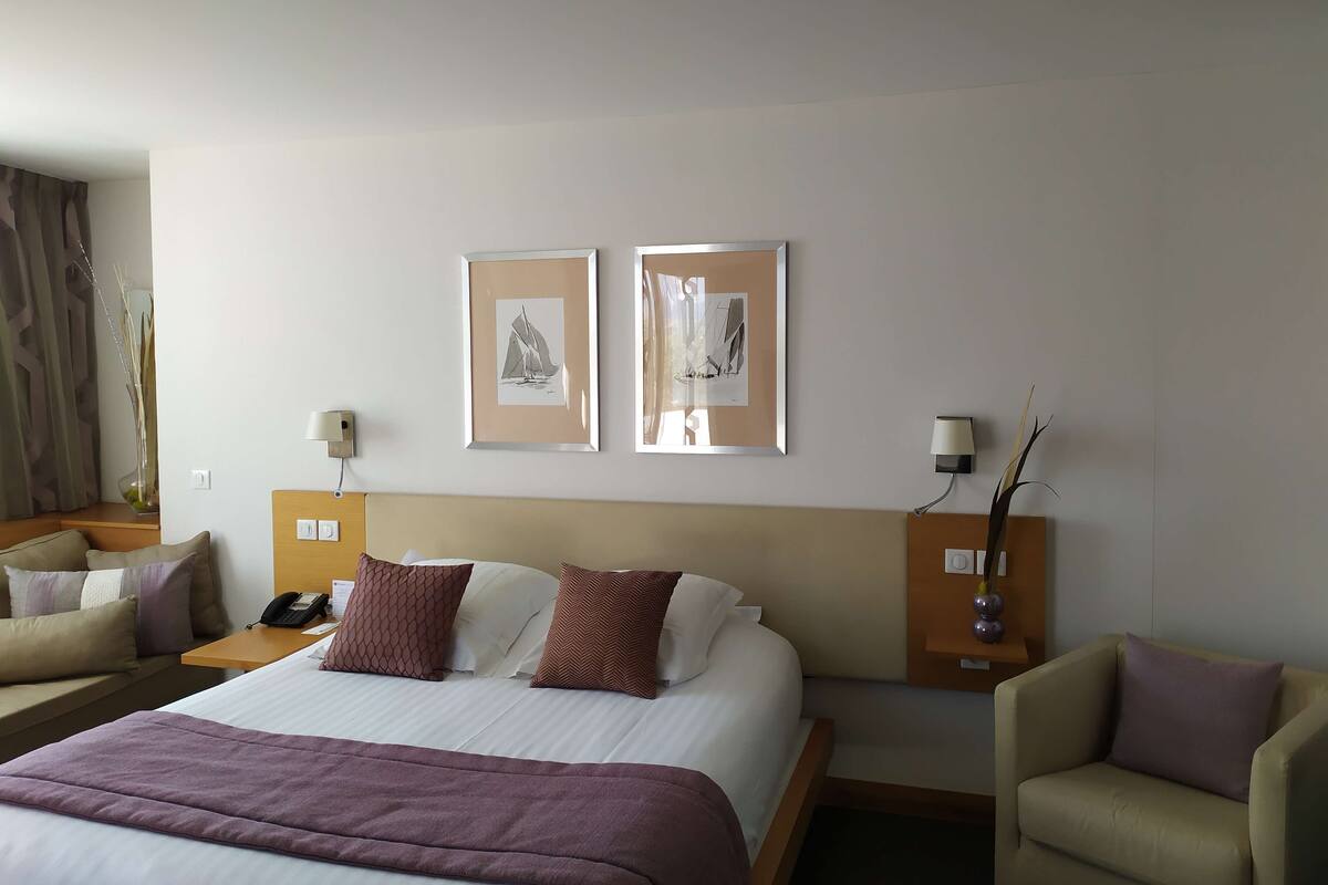 A hotel room with a bed, two bedside tables with lamps, a chair, and two framed pictures on the wall.
