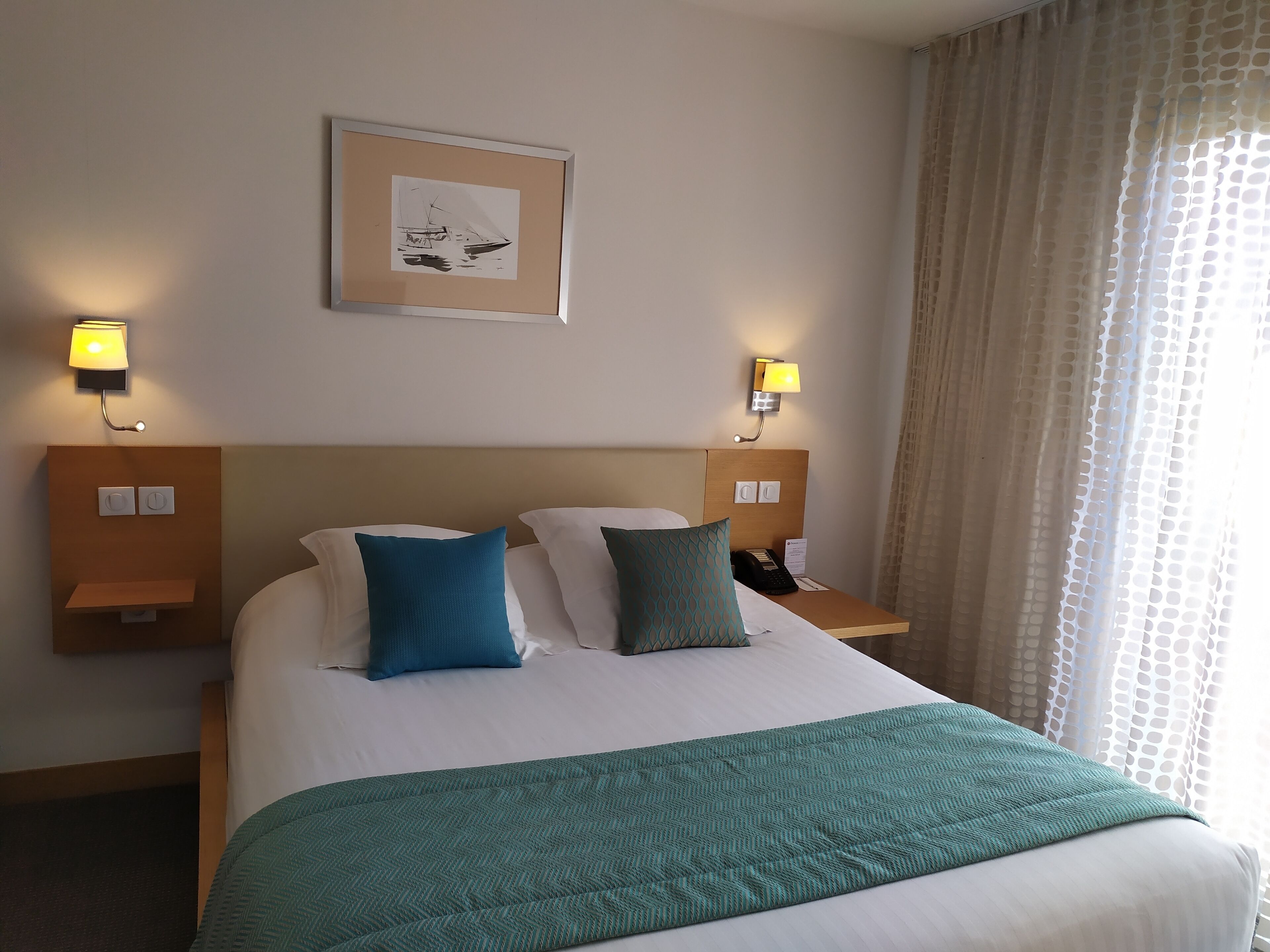Habitación de hotel con una cama grande, dos lámparas de noche, un cuadro en la pared y una ventana con cortinas.
