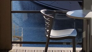 Un balcón con vistas a un yate grande amarrado en un puerto deportivo, una silla blanca y una barandilla.