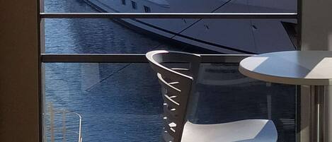 A balcony with a view of a large yacht docked at a marina, a white chair, and a railing.