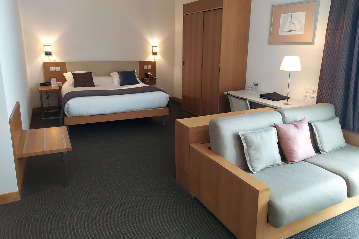 A hotel room with a bed, a desk, a sofa, and a wardrobe.
