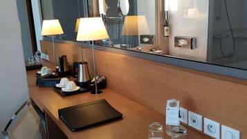 A modern hotel bathroom with a large mirror, two wall-mounted lamps, a sink, and a shower.