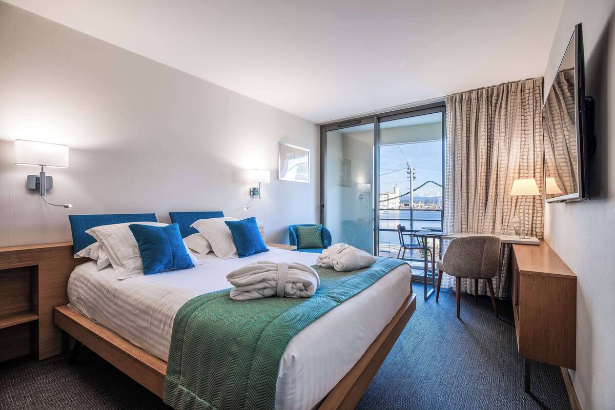 A hotel room with a bed, a desk, a chair, and a view of the outside.