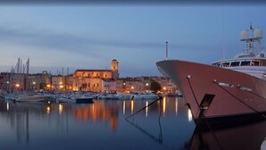 Un puerto deportivo con barcos amarrados, un edificio grande con una torre y agua tranquila que refleja las luces.